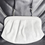 Load image into Gallery viewer, A white leather clutch bag with a subtle embossed geometric pattern, featuring a black shoulder strap and silver-tone hardware, displayed on a dark gray textured leather background.
