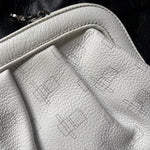 Load image into Gallery viewer, Close-up of a light white pebbled leather bag with a repeating black geometric line pattern, featuring a silver zipper pull on a dark textured background.

