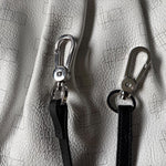 Load image into Gallery viewer, Two silver metal swivel snap clips attached to black leather wristlet straps, displayed on a textured white leather surface with a faint geometric grid pattern.

