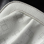 Load image into Gallery viewer, Close-up of a white pebbled leather or faux leather material with visible stitched edge and faint geometric line patterns, set against a dark black textured background.
